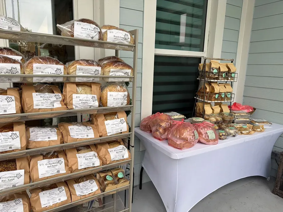 The Seaside Sourdough porch stand: a rack full of labeled sourdough loaves and a table of cookies, muffins and treats